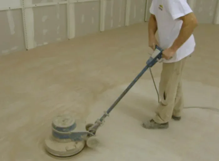 Un ouvrier ponce une chape à la monobrosse dans un local en travaux