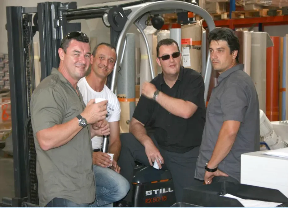 Quatre membres de l'équipe posent devant un chariot élévateur et les rayonnages de l'entrepôt, en 2009